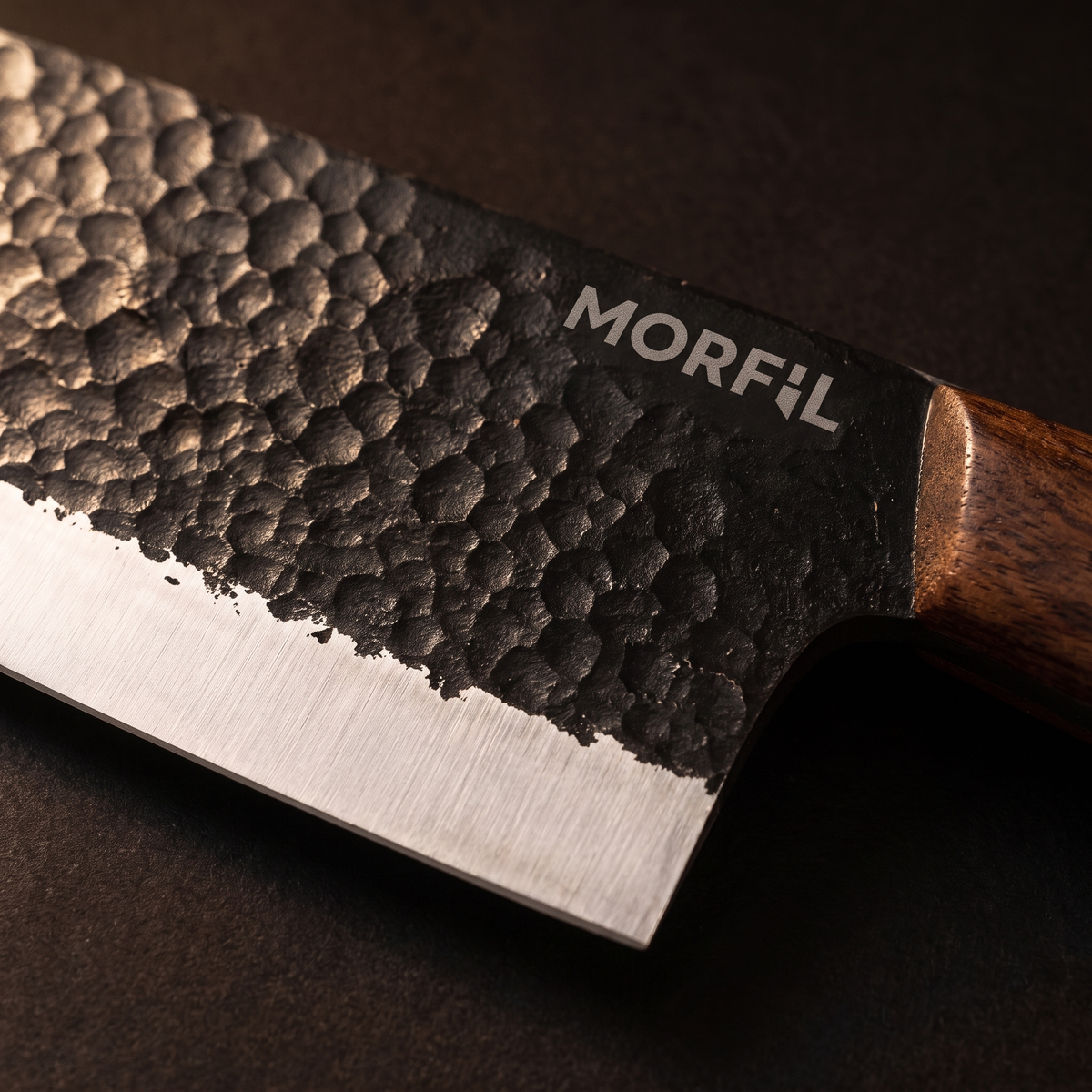 Gros plan sur le flanc martelé noir de la lame de Fournaise, son biseau satiné et le logo Morfil gravé