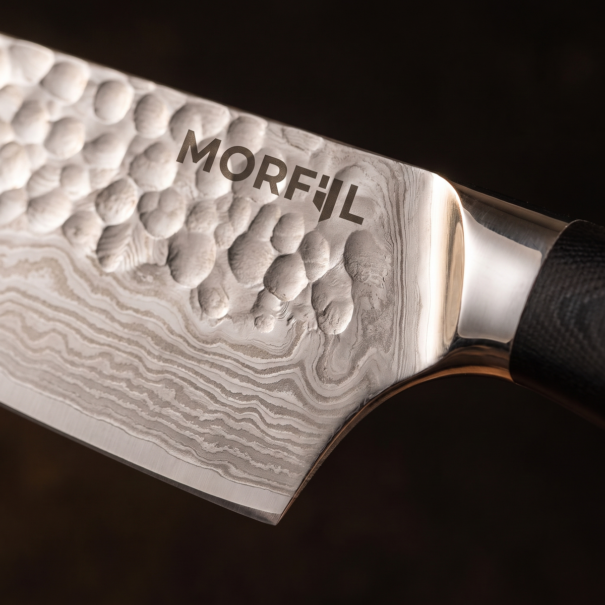 Gros plan sur la lame de Foyer : martelage en haut, motif ondulé en bas, mitre inox et logo Morfil gravé